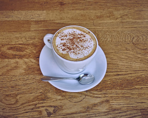 Cappuccino in white cup close-up on wood background