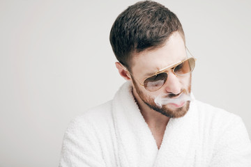 A bearded man in a bathrobe and glasses exhales