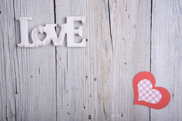 Word LOVE and paper heart on old wooden background