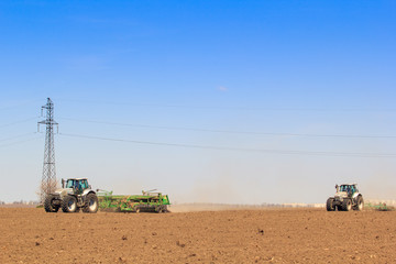 view of two tractors sowing in field in spring