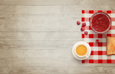 Fruit breakfast with free space for text on wooden table. Jar of jam, raspberry, tea, orange,...