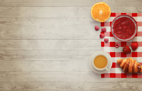 Fruit breakfast with free space for text on wooden table. Jar of jam, strawberry, raspberry, juice, apple, orange, tablecloth, muffin, croissant, wooden table with top view.