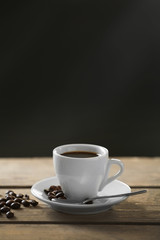 Cup of coffee and coffee grains on wooden table, on gray background