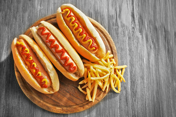 Delicious hot-dogs with French fries on wooden chopping board, close up