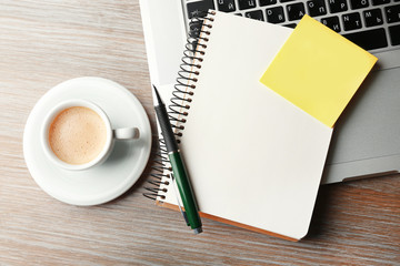 Empty yellow adhesive paper, notebook on laptop keyboard, pen and coffee cup on desk background