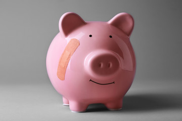 Piggy Bank with adhesive bandage on grey background
