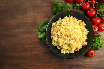 Stewed rice with a carrot on a black plate over wooden background