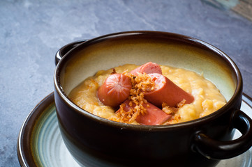 Bowl of yellow split pea soup with chopped hot dog sausage and fried onion. A popular Scandinavian dish served on a slate table.
