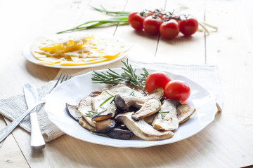 Fototapeta na wymiar Fried eryngii mushrooms with fresh rosemary in white plate on wooden background