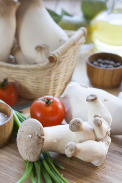 Eryngii mushrooms, olive oil and ingredients for cooking on the wooden table of the kitchen background