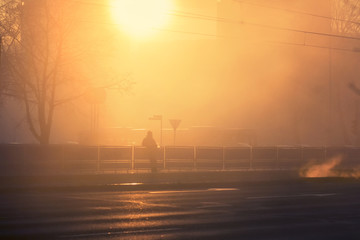 Foggy sunset on a city streets with silhouette of a lonely man on a tram station