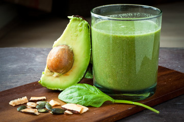 Healthy breakfast vegetable smoothie made from spinach and avocado blended with coconut milk. Served on a wooden tray on a slate stone table.