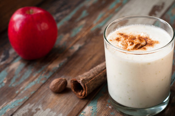 Apple crumble smoothie milkshake topped with cinnamon and nutmeg spices. Served on a rustic wooden table.