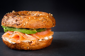 Healthy freshly baked bagel filled with smoked salmon lox and topped with avocado. Served on a gray...