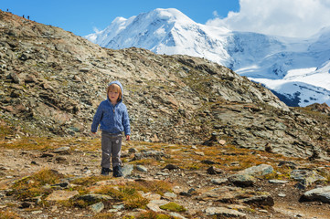 Naklejka na ściany i meble Cute kid boy resting in Alps, wearing warm knitted jacket and mountain boots