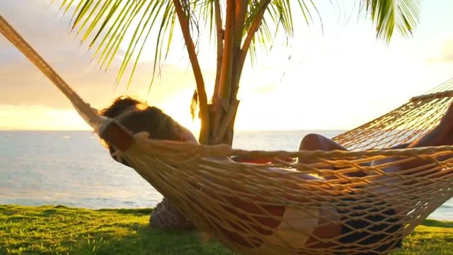Romantic couple relaxing in tropical hammock at sunset. Summer Luxury Vacation. SLOW MOTION. 