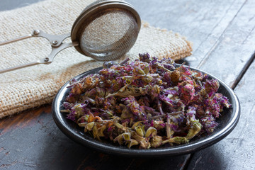 Salvia for making herbal tea on a black saucer and a strainer for brewing tea on the matting on the old black boards. Top view close-up. Selective focus. Rustic style. concept of alternative medicine