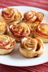 Fototapeta na wymiar Fresh puff pastry with apple shaped roses on red wooden table