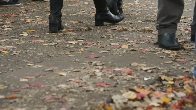 Feet of people walking along a sidewalk with many fallen leaves in Autumn