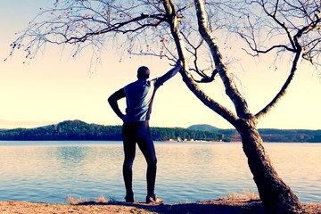 Silhouette of sport active man in running leggins and blue shirt at birch tree on  beach. Calm water, island and sunny day