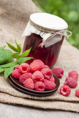 Raspberry preserve in glass jar and fresh raspberries on a plate