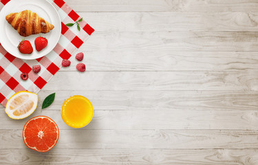 Fruit breakfast with free space on wooden table. Croissant, orange, raspberries, juice, with top view.