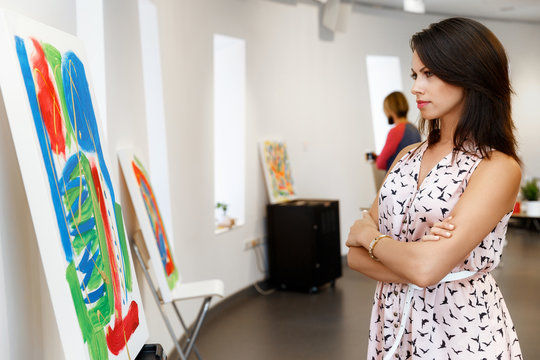 Young caucasian woman standing in art gallery front of  paintings