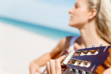 Beautiful young woman playing guitar on beach