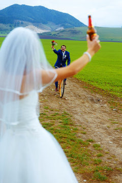 bride with a beer bottle and a groom on bicycle on the background - wedding concept.