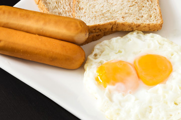 Fried eggs with sausages and bread on the white plate