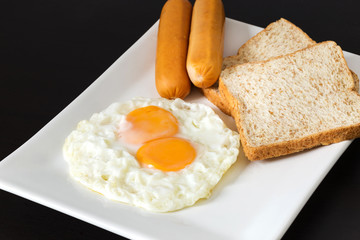 Fried eggs with sausages and bread on the white plate