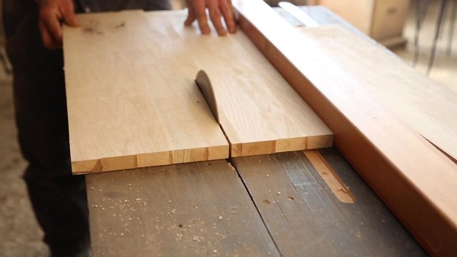 Carpenter sawing plank on a saw circulation in workshop