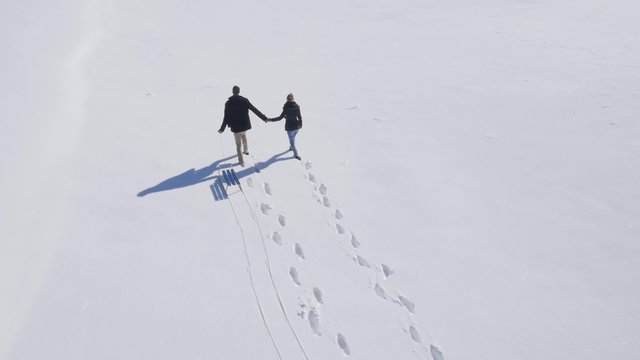 Aerial view on young couple enjoy walking on the snow during calm sunny winter day.
