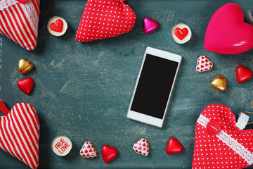 top view image of smartphone, colorful heart shape chocolates, fabric hearts on blackboard background. valentine's day celebration concept
