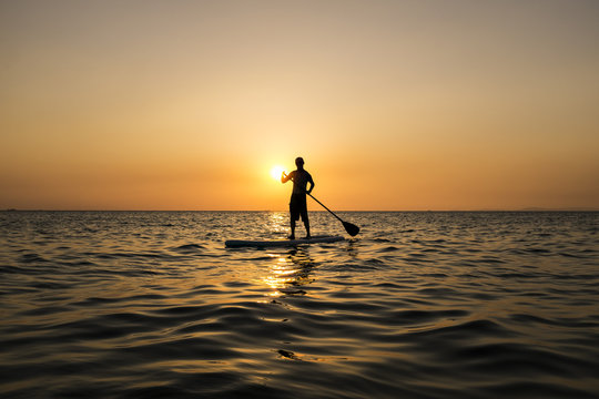 Man paddling while standing on a surfboard in the sunset, Otres Beach, Cambodia.