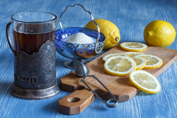 Натюрморт: стакан чая, ваза с сахаром и лимоны на деревянном столе