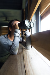 Woman using binoculars for birdwatching at wooden house