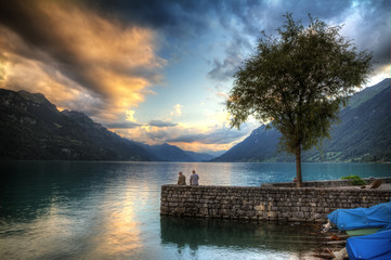 Fototapeta premium Two old men are fishing on the shore of the brienzersee in Switzerland at sunset. HDR