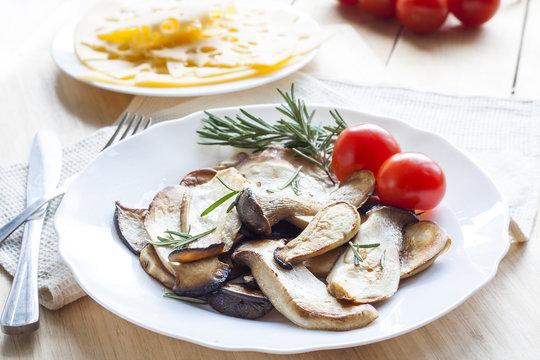 Fried eryngii mushrooms with fresh rosemary in white plate on wooden background