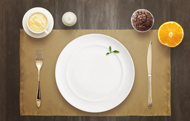 Empty plate on the table waiting for serving. Top view of tablecloth, muffin, orange, coffee.