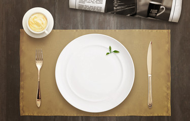 Empty plate on the table waiting for serving. Top view of tablecloth, newspaper, coffee.