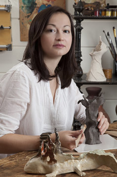 Woman sculpts from raw clay the flower vase