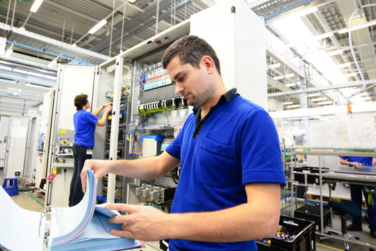 Mitarbeiter in einer Elektronikfabrik kontrolliert techn. Unterlagen zur montage von Bauteilen