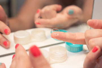 Female hands holding lens, lens case in background, in front of mirror