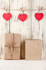 Gift box and cardboard bag with heart-shaped tags on wooden back