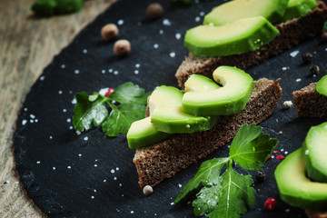 Sandwich with avocado, black rye bread and spices on dark stone