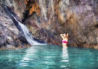 Gorgeous, young woman in magenta swimwear having a recreation nearby waterfall.