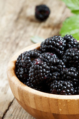 Beautiful ripe black blackberries in wooden bowl with leaves, se