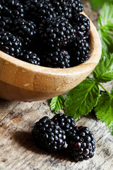 Beautiful ripe black blackberries in wooden bowl with leaves, se