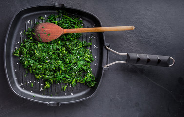 Preparing fresh spinach with salt on frying pan